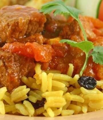 Close-up of beef vindaloo curry with spiced yellow rice garnished with cilantro and raisins