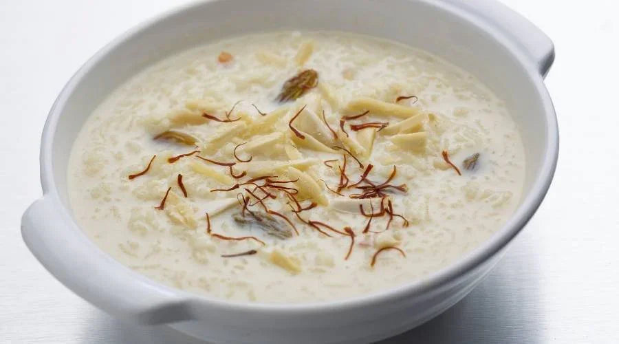 White bowl of rice kheer garnished with saffron strands and dry fruits on white surface