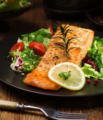 Grilled salmon fillet garnished with rosemary and lemon slice, served with fresh mixed salad on black plate