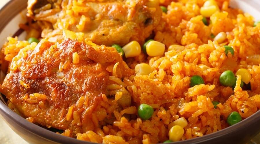 Close-up of Brazilian Galinhada with seasoned chicken thighs, yellow corn, green peas, and orange rice in a bowl