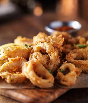 Golden fried calamari rings on wooden board with small bowl of red dipping sauce in background