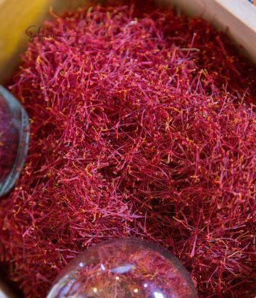 Close-up of vibrant red saffron threads drying in a wooden tray under glass weights