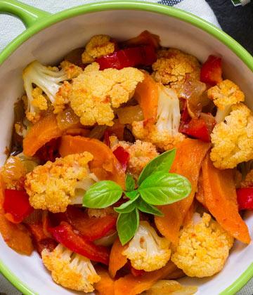 Bowl of cooked cauliflower and red bell peppers garnished with fresh basil leaves
