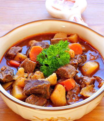 Hearty beef goulash stew with carrots, potatoes, and parsley garnish in ceramic bowl