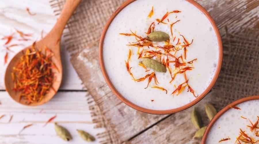 Persian saffron milkshake in clay bowl topped with saffron strands and cardamom pods on rustic wooden table