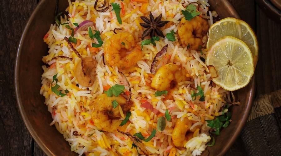 Close-up of prawn biryani with spices, herbs, lemon slices in a rustic bowl on dark surface