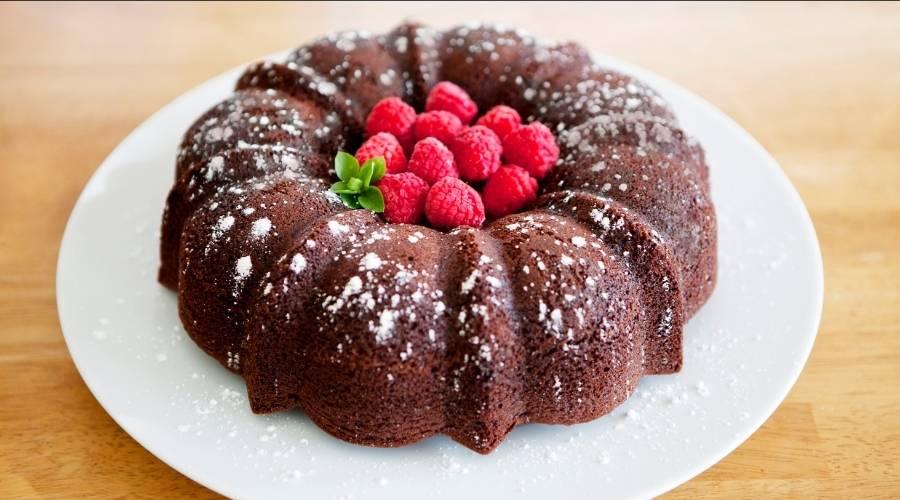 Chocolate Bundt cake dusted with powdered sugar and topped with fresh raspberries on white plate
