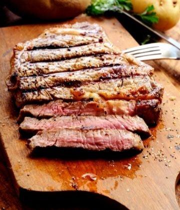 Grilled medium-rare steak sliced on a wooden cutting board with pepper seasoning