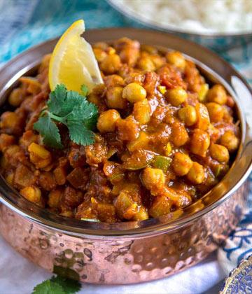 Close-up of spicy chickpea curry garnished with lemon wedge and cilantro in a hammered copper bowl