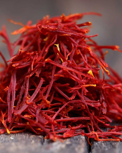 Close-up of vibrant red saffron threads on wooden surface, highlighting spice texture
