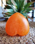 Heart-shaped saffron soap bar with orange speckled texture on woven surface and green plant background